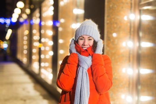Girl having fun christmas decoration lights street. Young happy smiling woman wearing stylish knitted scarf and jacket outdoors. Model laughing. Winter wonderland city scene, New Year party.