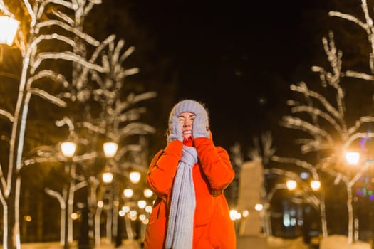 Happy funny young woman with winter clothes background evening city lights illumination. Christmas and winter holidays.