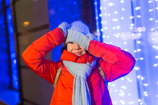 Girl having fun christmas decoration lights street. Young happy smiling woman wearing stylish knitted scarf and jacket outdoors. Model laughing. Winter wonderland city scene, New Year party.