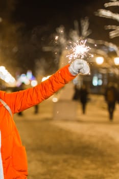 Young beautiful woman in knitted hat and scarf standing in the city with bengal light, sparkler. Concept celebration and christmas