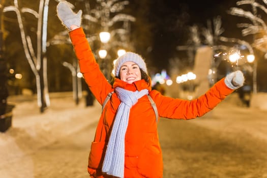 Young beautiful woman in knitted hat and scarf standing in the city with bengal light, sparkler. Concept celebration and christmas