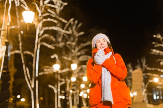 Happy funny young woman with winter clothes background evening city lights illumination. Christmas and winter holidays.