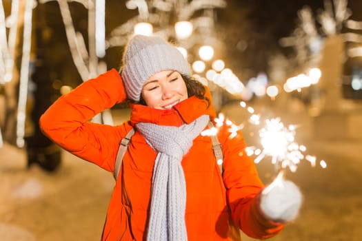 Girl holding a sparkler in her hand. Outdoor winter city background, snow, snowflakes