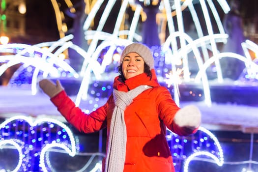 Girl holding a sparkler in her hand. Outdoor winter city background, snow, snowflakes