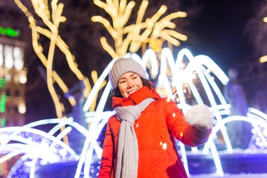 Girl holding a sparkler in her hand. Outdoor winter city background, snow, snowflakes