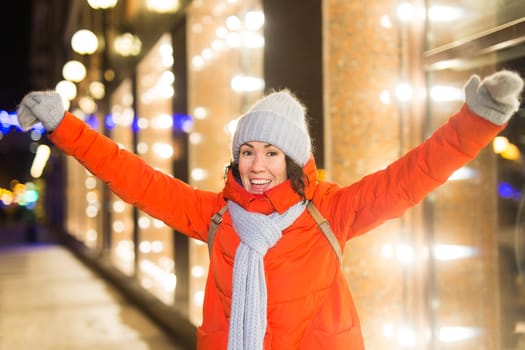 Winter holiday season. Christmas, New Year concept. Funny woman spend time having fun near illuminated and decorated showcase on city street.
