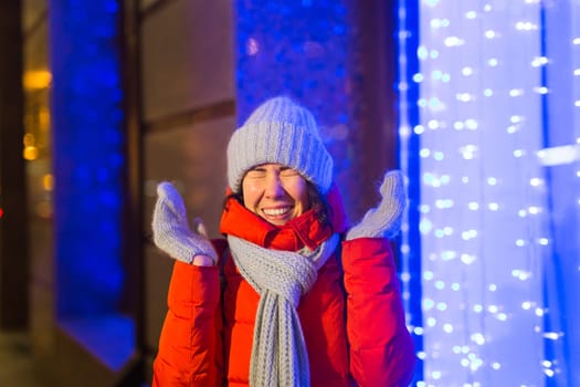 Winter holiday season. Christmas, New Year concept. Funny woman spend time having fun near illuminated and decorated showcase on city street.