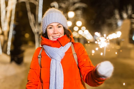 Girl holding a sparkler in her hand. Outdoor winter city background, snow, snowflakes