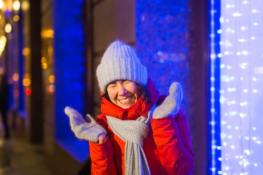 Happy funny young woman with winter clothes background evening city lights illumination. Christmas and winter holidays.