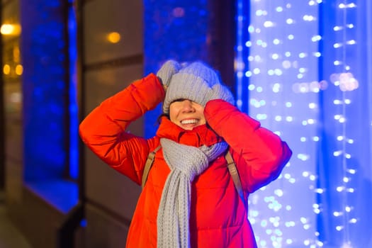 Winter holiday season. Christmas, New Year concept. Funny woman spend time having fun near illuminated and decorated showcase on city street.