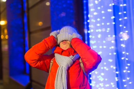 Happy funny young woman with winter clothes background evening city lights illumination. Christmas and winter holidays.