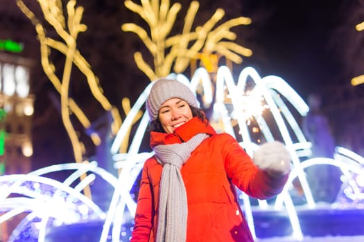 young woman wearing winter knitted clothes holding sparkler outdoors over snow background. Christmas holidays.