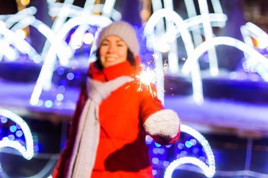 Girl holding a sparkler in her hand. Outdoor winter city background, snow, snowflakes