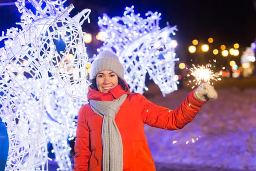 Girl holding a sparkler in her hand. Outdoor winter city background, snow, snowflakes