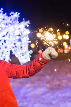 Young beautiful woman in knitted hat and scarf standing in the city with bengal light, sparkler. Concept celebration and christmas