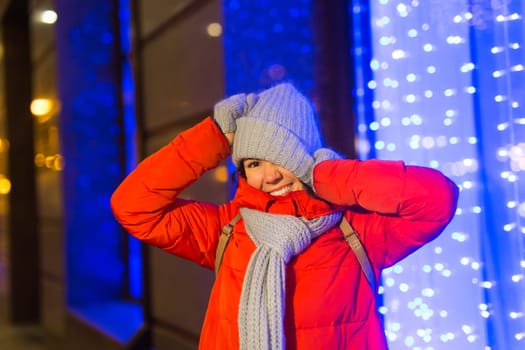 Happy funny young woman with winter clothes background evening city lights illumination. Christmas and winter holidays.