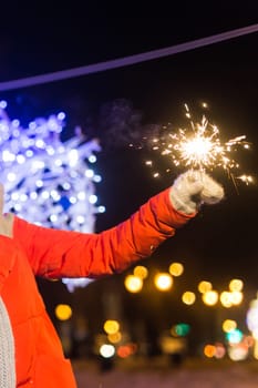 Girl holding a sparkler in her hand. Outdoor winter city background, snow, snowflakes