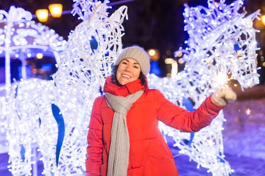 Girl holding a sparkler in her hand. Outdoor winter city background, snow, snowflakes