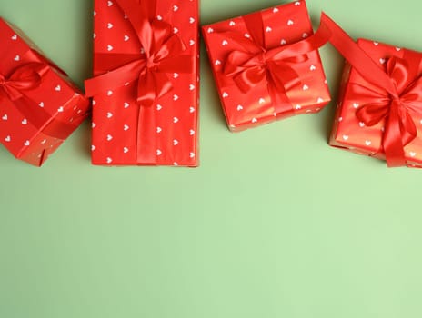 Boxes packed in red paper and tied with ribbon on a green background, gifts. Copy space