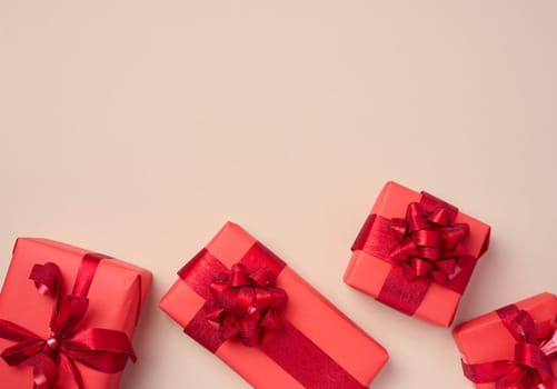 Boxes packed in red paper and tied with ribbon on a beige background, gifts