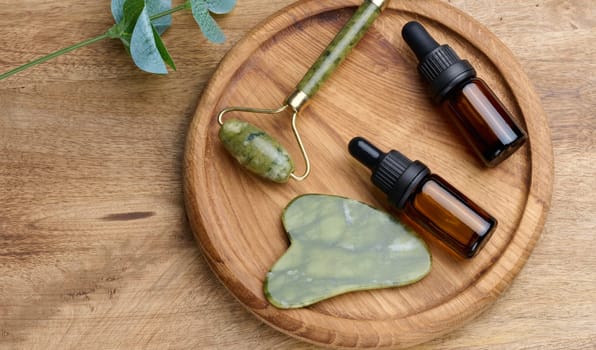 Brown glass bottle with a pipette,  stone hand massager for cosmetic procedures on a wooden background, top view