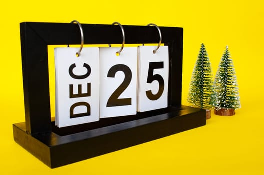25 December calendar with Christmas trees on yellow background. Christmas season concept.