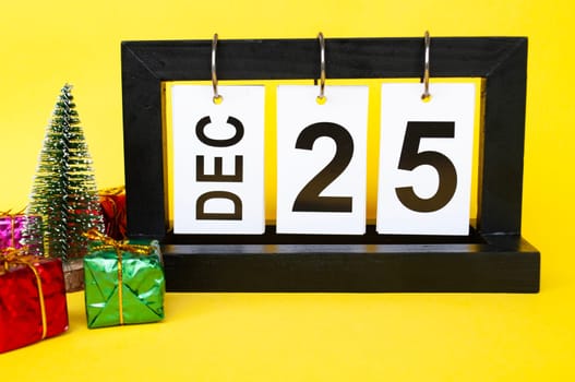 25 December calendar with Christmas tree and presents on yellow background. Christmas concept.