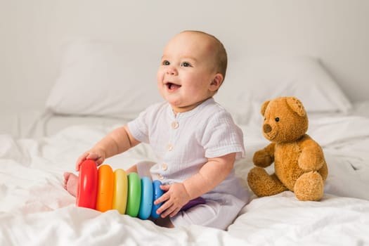 Baby boy in white bedroom. Newborn child in bed with toys. Nursery for children. Textile, pillows and bedding for kids. Family morning at home. New born kid time with toy bear