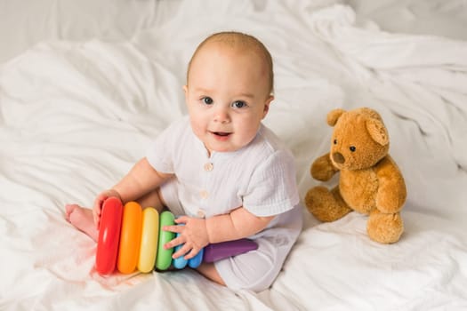 Baby boy in white bedroom. Newborn child in bed with toys. Nursery for children. Textile, pillows and bedding for kids. Family morning at home. New born kid time with toy bear