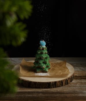 Beautiful gingerbread tree, decorated with icing, with caramel toys on a dark background with powdered sugar. New year gift. High quality photo