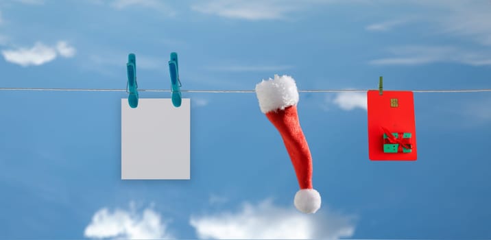 rope on which a plastic card, Santa hat and postcard hang against the blue sky. selective focus
