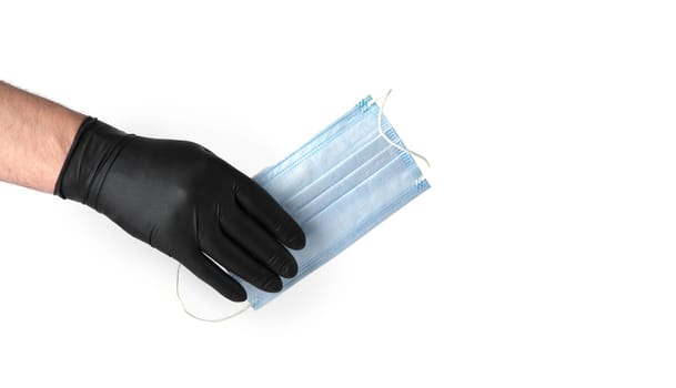 hand in black latex glove holds a disposable medical mask on a white background. selective focus