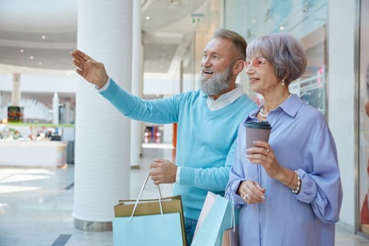 Happy elderly couple in shopping mall going for Black Friday sales. Happy retirement, price clearance and discounts concept