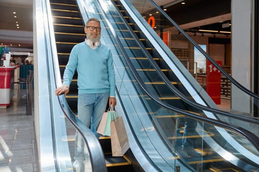 Handsome senior man holding shopping bags and smiling while walking in mall