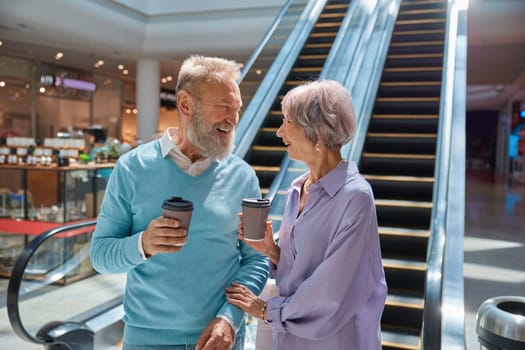 Excitedly laughing senior couple talking and sharing positive expression during shopping time in city mall