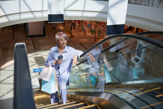 Happy retired woman riding on escalator at shopping mall anticipating big discounts and sales on Black Friday