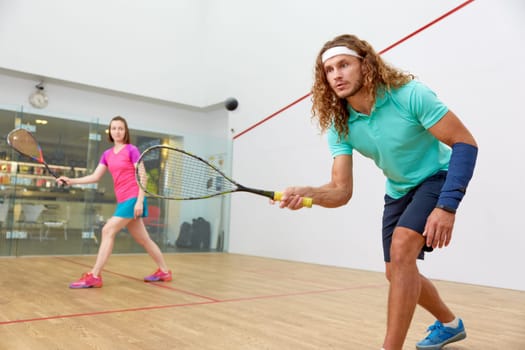 Couple holding squash racquets playing game match at fitness studio. Athletic man and woman recreation