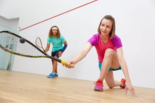 Young sportive couple practicing squash at sport club indoor court. Focus on attractive woman hitting ball with racket