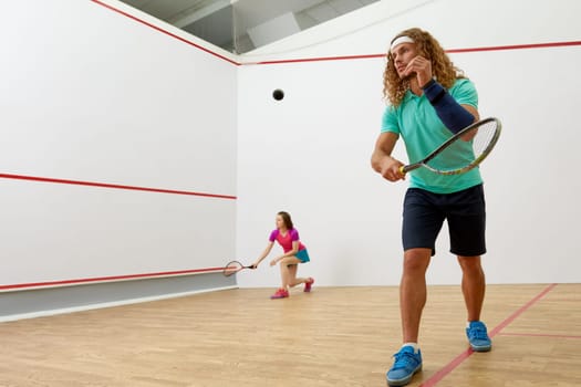 Happy millennial-age couple characters playing game of racquetball together. Squash player training together at indoor court