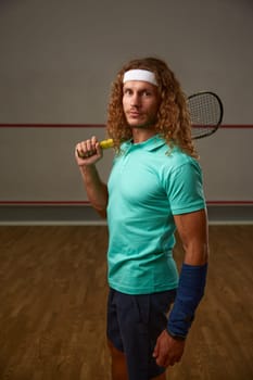 Portrait of male squash player standing with racket ready for game looking confidently at camera