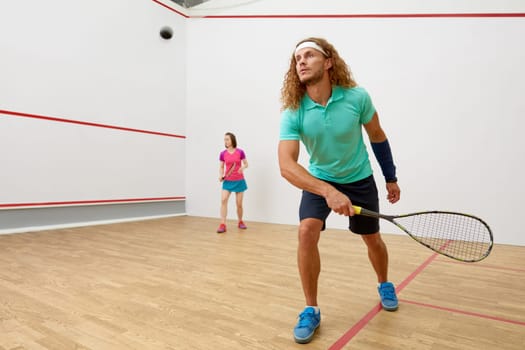Squash male player with racket playing game with female friend at indoor training court