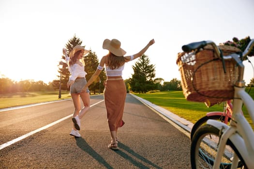 Young female friends enjoying road trip on bicycle spending weekend together. View on excited joyful teenager girls running on road and bike parked at sidewalk