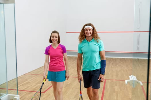 Satisfied man and woman athlete after successful squash game. View from glass sportive club doorway