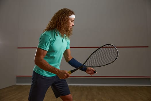 Young adult concentrated squash player practicing serve while exercising game at gym. Sportsman portrait