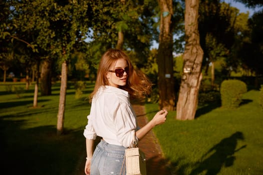 Outdoor portrait of young pretty woman walking in park at sunny day. Happy cheerful teenager girl with look fashion turning with her back to camera