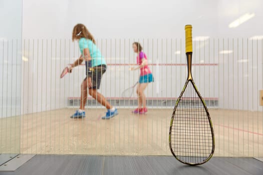 Squash game concept with racket leaned on net and sportspeople playing together on blurred background. Professional high quality equipment for racquetball training
