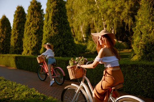 Stunning young females laughing riding bicycle and having fun in urban park. Excited positive teenager girls friends enjoying walk and summer season