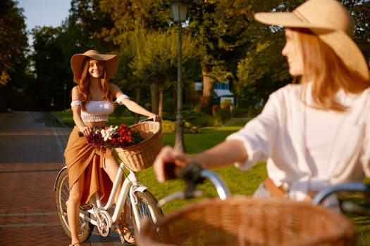 Two young women riding bicycle in urban park. Active leisure activity, youth and healthy lifestyle