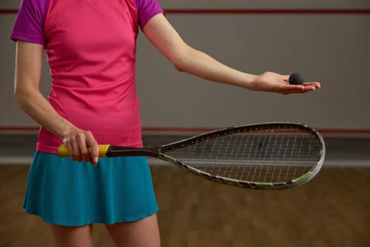 Closeup cropped view on female squash player holding racket and ball in hand. Recreational pursuit with professional game equipment