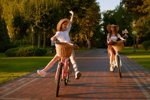 Happy funny young girl with female friend riding on bicycle with raised legs. Fun student leisure activity and friendship people relations